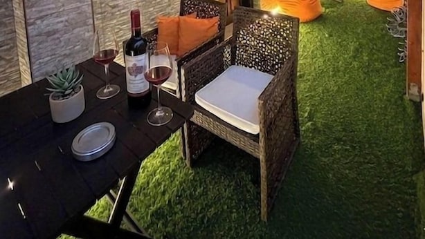 Un patio al aire libre con una mesa de comedor, sillas y una botella de vino.
