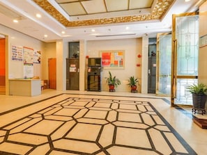 Un'ampia hall con pavimento a motivi geometrici, una reception, piante in vaso e un'ampia finestra con vetrata decorativa.