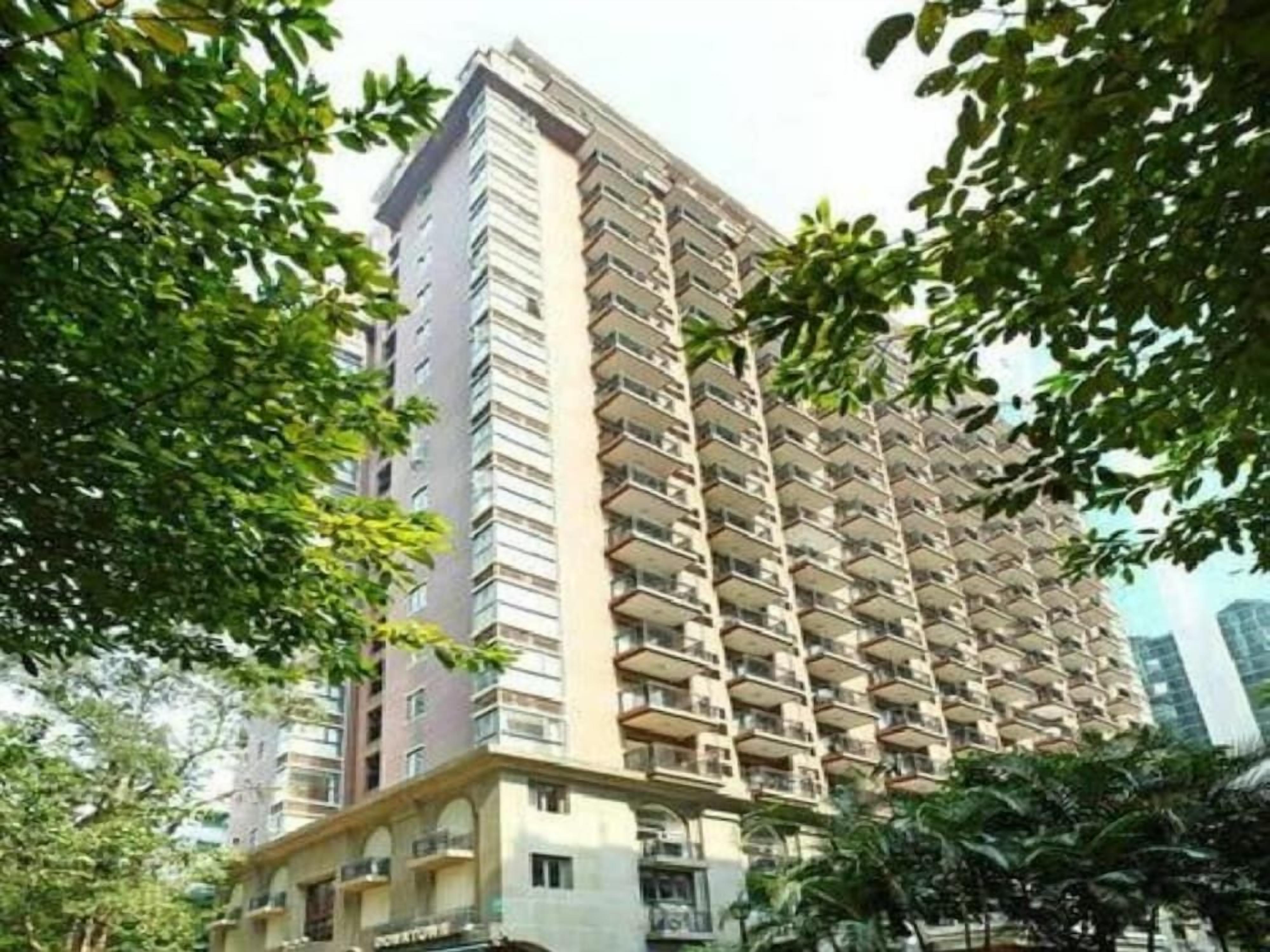 A high-rise residential building with multiple balconies, surrounded by trees.