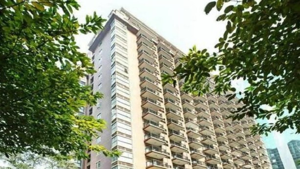 Un edificio residencial de gran altura con varios balcones, rodeado de árboles.