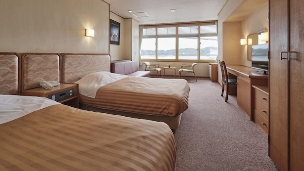 Habitación de hotel con dos camas, un escritorio, una silla, un televisor y ventana con vistas.