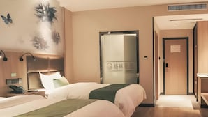 Ett hotellrum med två sängar, ett nattduksbord med en telefon, en väggmonterad lampa och en dörr med en skylt.