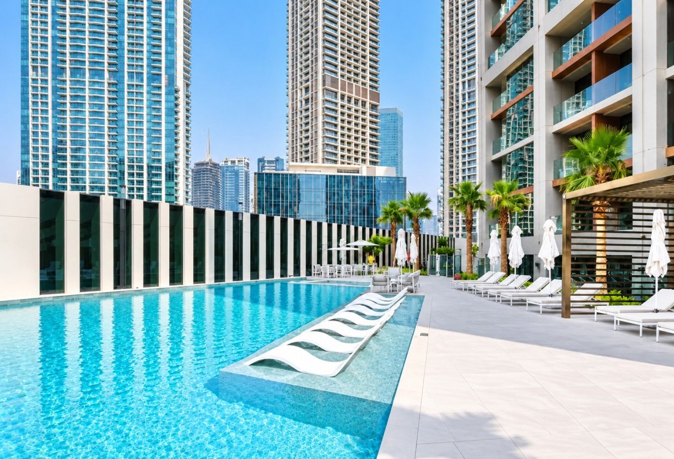Una piscina moderna con sillas de descanso y sombrillas, rodeada de edificios altos.