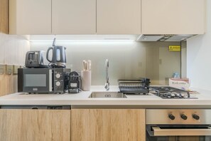 Eine moderne Küche mit Mikrowelle, Kaffeemaschine, Toaster und Wasserkocher. Es gibt ein Spülbecken mit Armatur, einen Geschirrständer und eine mit 'Willkommen' beschriftete Box.