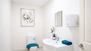 Een badkamer met toilet, wastafel, spiegel en een wanddecoratie met bloemen.
