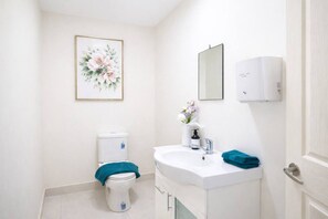 Et badeværelse med toilet, vask, spejl og et billedrammet blomstermotiv på væggen.