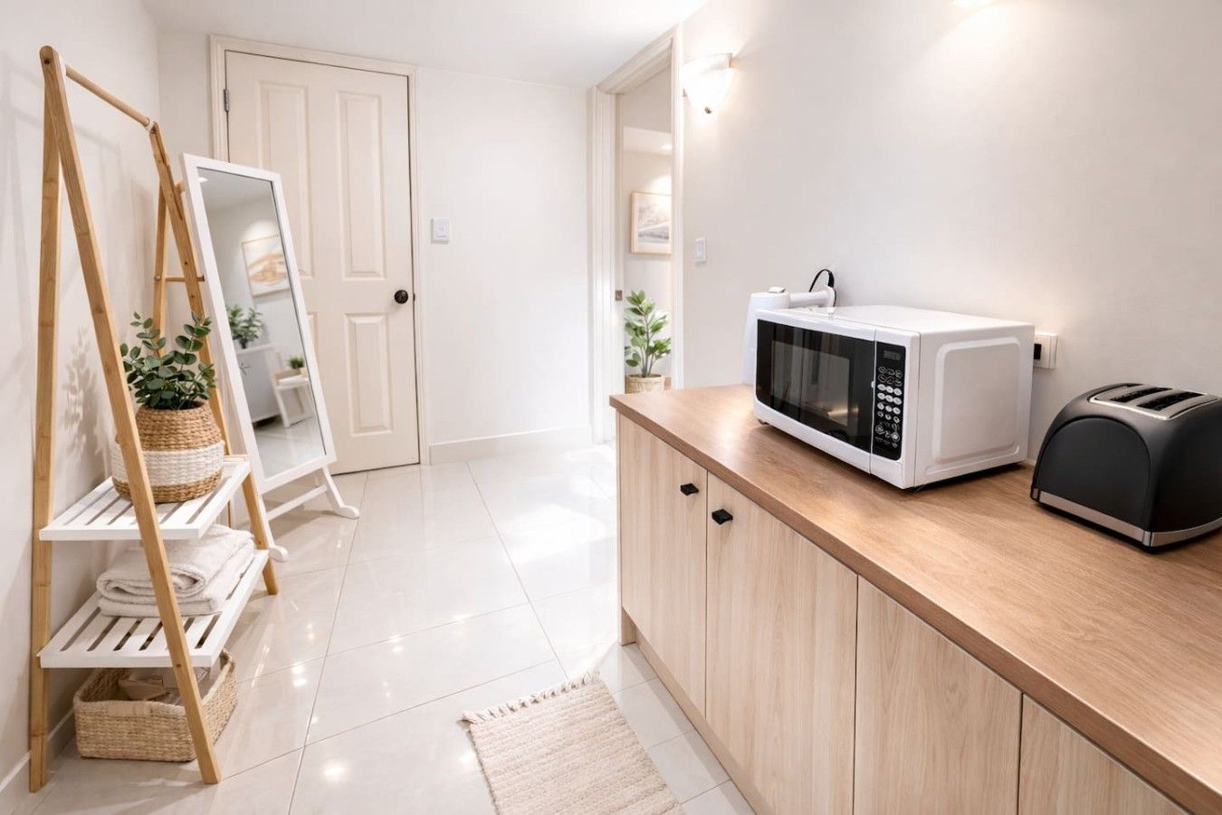 Une cuisine moderne équipée d’un four à micro-ondes, d’un grille-pain, de meubles en bois, d’une porte blanche et d’une plante posée sur une étagère en bois.