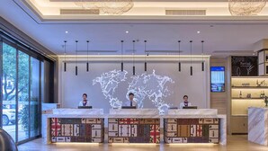 Un comptoir d’accueil d’hôtel avec un globe terrestre, trois réceptionnistes et un bar avec des bouteilles exposées.