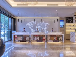 Un mostrador de recepción de hotel con una proyección de mapa mundial, tres recepcionistas y una zona de bar con botellas.