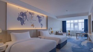 Une chambre d’hôtel avec deux lits, un bureau, une chaise, une carte du monde accrochée au mur et une vue sur la ville.