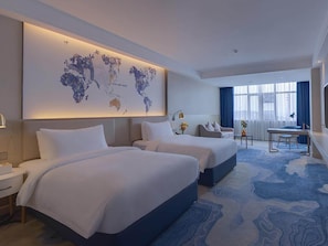 Habitación de hotel con dos camas, un escritorio, una silla, un mapa mundial en la pared y vista a la ciudad.
