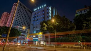 Un hotel de varios pisos con letreros iluminados, rodeado de infraestructura urbana y una calle con movimiento.