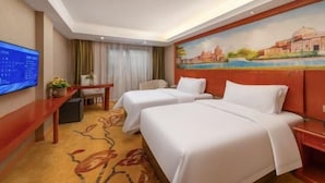 Quarto de hotel com duas camas, televisão de tela plana, escrivaninha com cadeira e um quadro na parede.