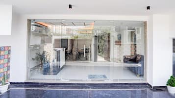Entrada de un edificio moderno con puerta de cristal, suelo de baldosas y plantas en macetas.