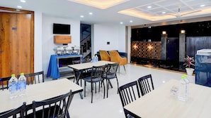 Un comedor moderno con mesas y sillas, un televisor montado en la pared, y una escalera que conduce a un nivel superior.