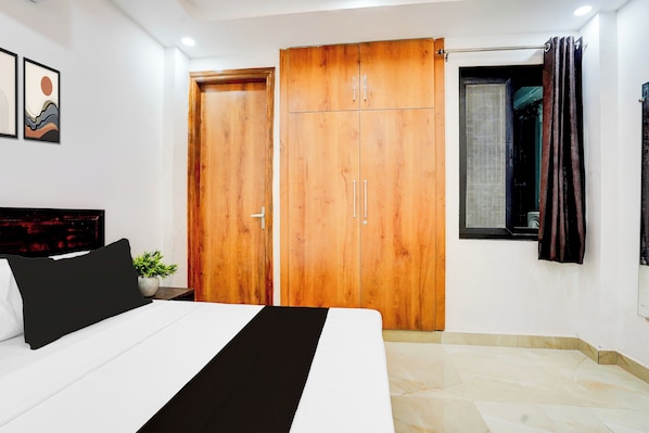 Un dormitorio con cama, armario, ventana con cortinas y una planta en maceta.