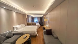 Quarto de hotel com sofá, duas camas, uma mesinha e um abajur.