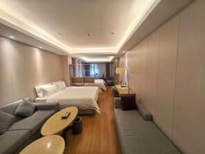 Una habitación de hotel con un sofá, dos camas, una mesita y una lámpara.