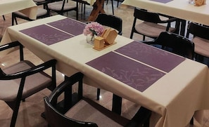 Un comedor con mesas dispuestas para el servicio, sillas y un jarrón con flores.