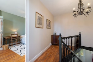 A staircase with a black balustrade leading to a landing, a chandelier, and two framed pictures on the wall. - Villa Serpentine Guest Room – Family Suite (Les Sables-d'Olonne)