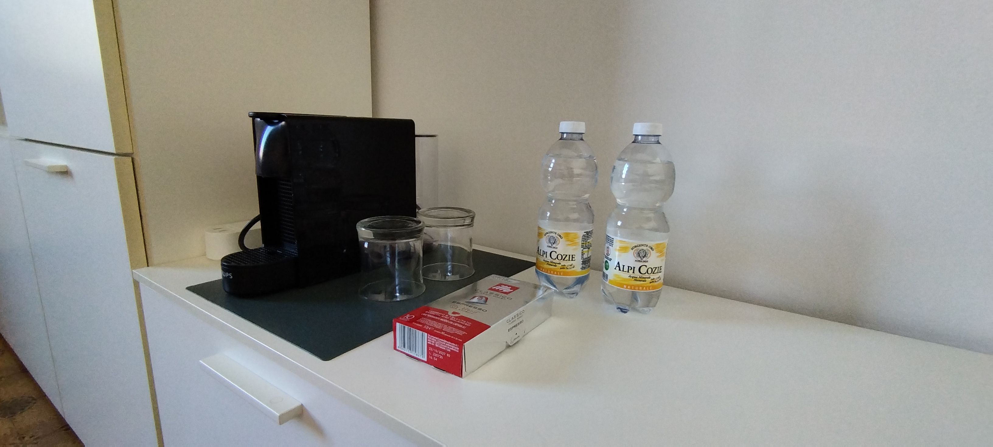 Angolo cottura con una macchina per il caffè, due bottiglie d'acqua, un bicchiere e una confezione di caffè.