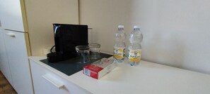 Une petite cuisine équipée d’une machine à café, de deux bouteilles d’eau, d’un verre et d’une boîte de café.