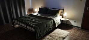 Un lit recouvert d’une couette vert foncé, deux lampes de chevet et un tapis à motifs.