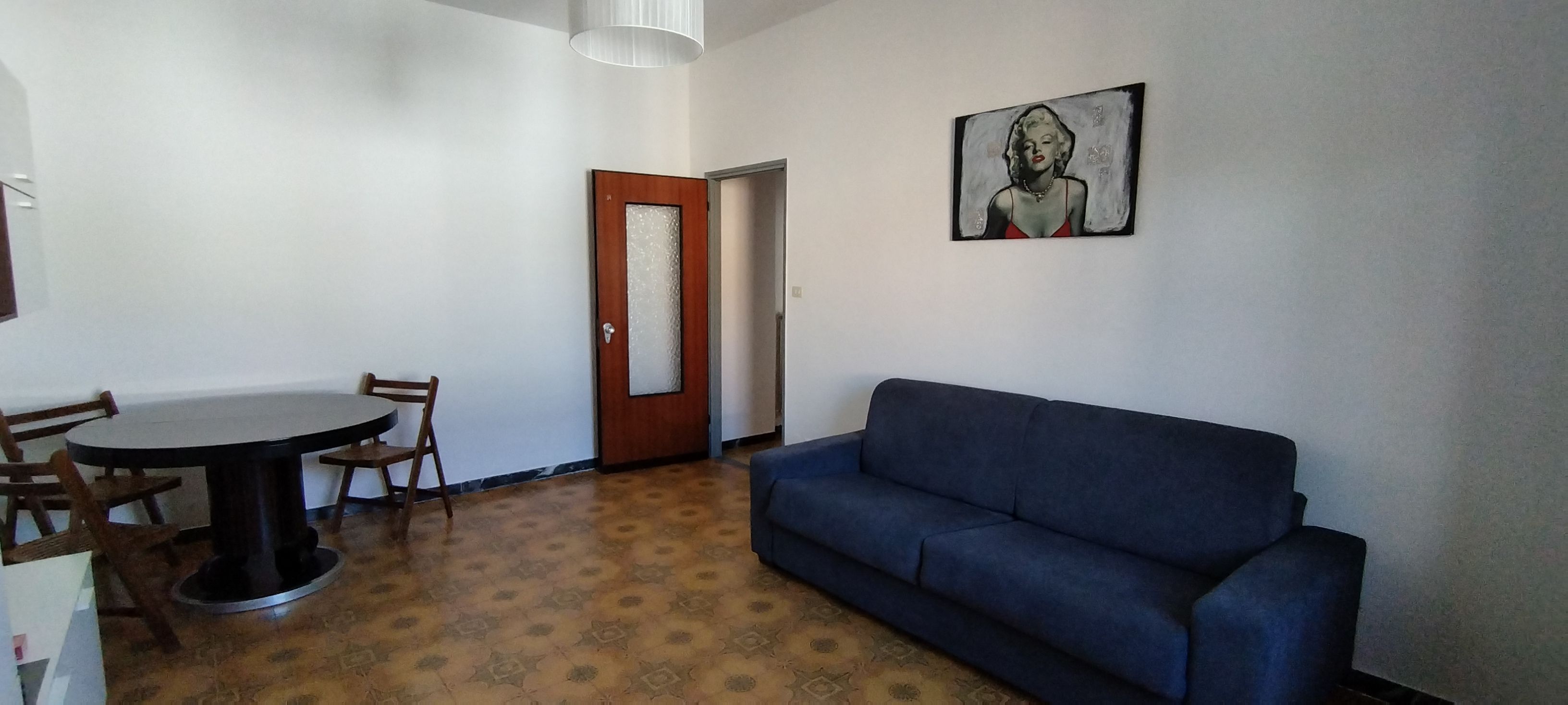 Una stanza con un divano blu, un tavolo da pranzo con sedie e una porta con un pannello di vetro smerigliato.