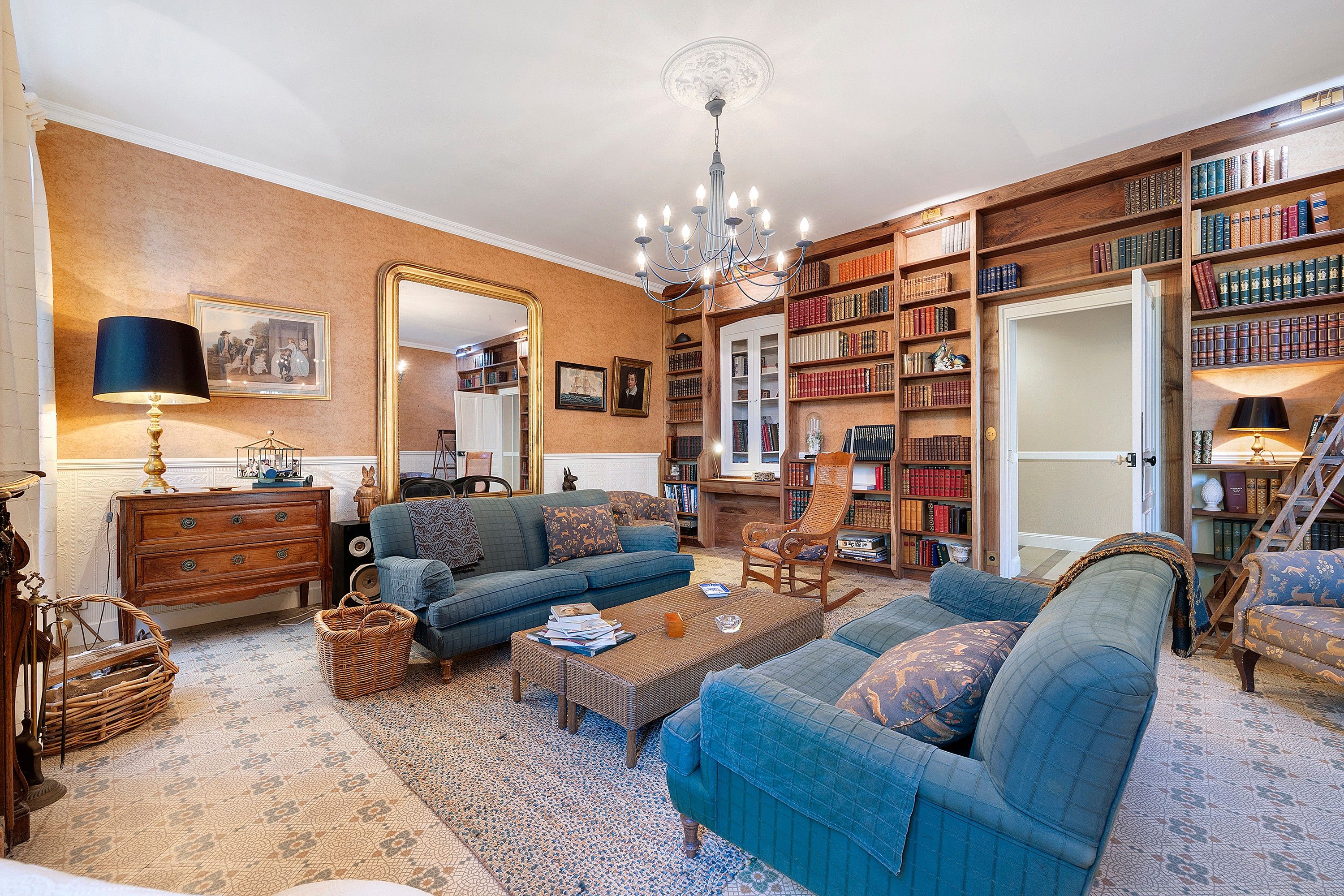 A spacious living room with a large bookshelf, a chandelier, and a comfortable seating area.