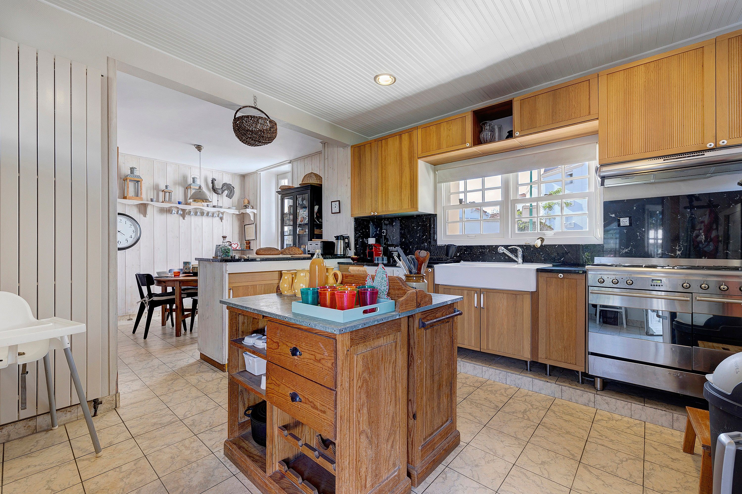 Une cuisine avec des meubles en bois, un îlot central, une cuisinière et un coin repas avec des chaises.