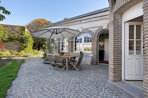 A patio area with a stone-tiled floor, a wooden table with chairs, and a large umbrella providing shade.