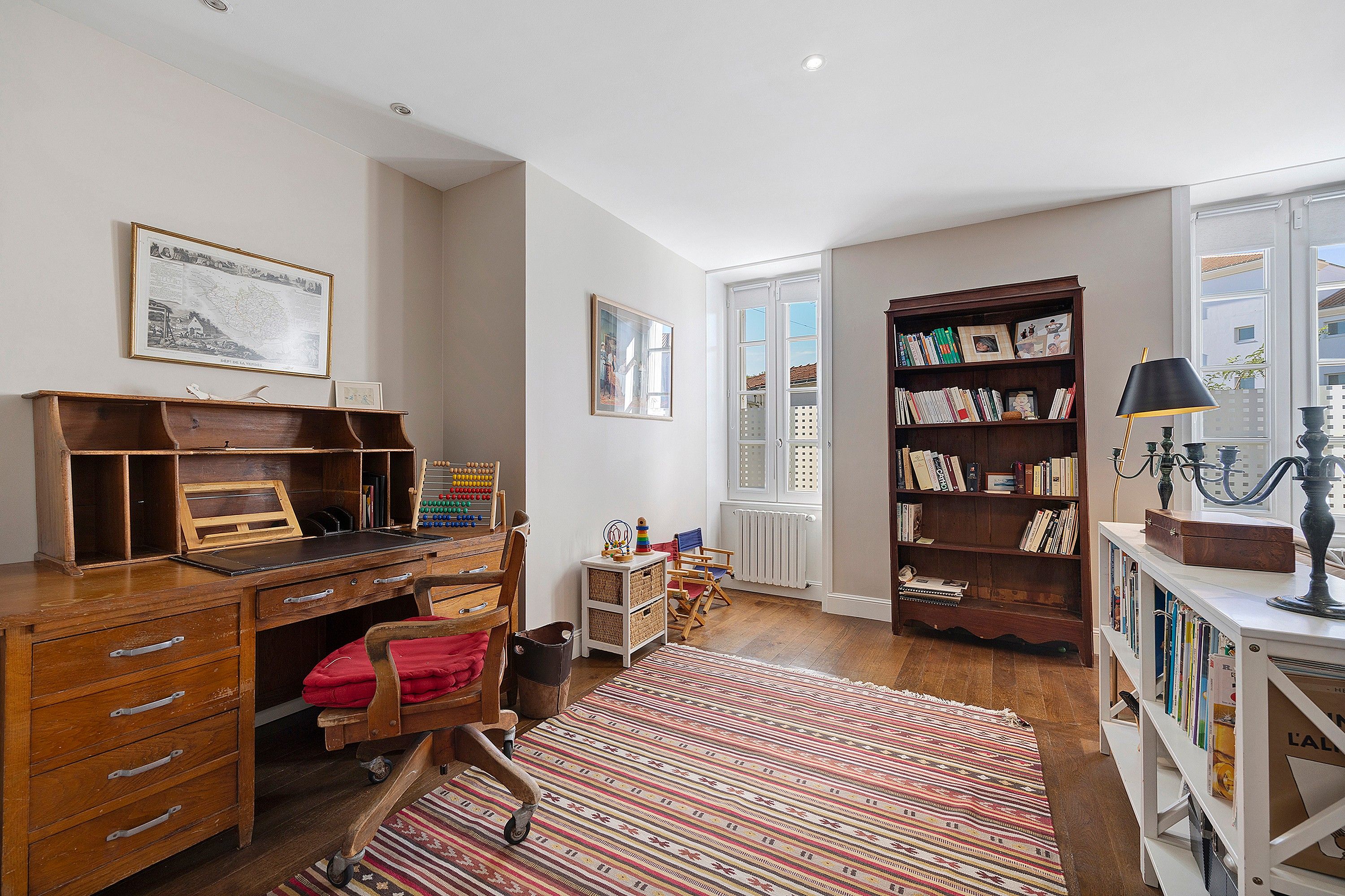 Une pièce avec un bureau en bois, une bibliothèque, un radiateur et une fenêtre.