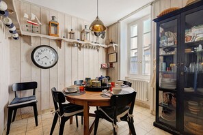 A dining area with a wooden table, chairs, a clock, and a cabinet with glass doors. - Villa Serpentine Guest Room – Parental Suite (Les Sables-d'Olonne)