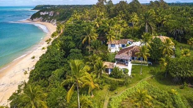 A coastal property with a beach, lush greenery, and two white buildings with thatched roofs. - Hotel Fazenda Cala and Divino (Porto Seguro)