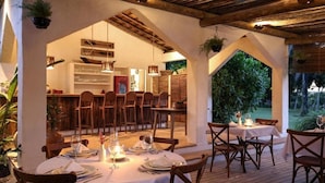 An outdoor dining area with round tables and chairs, a wooden ceiling, and a view of a lush garden. - Hotel Fazenda Cala and Divino (Porto Seguro)
