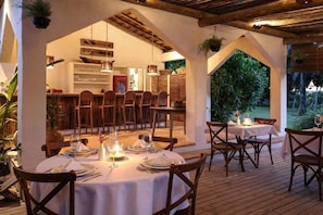 An outdoor dining area with round tables and chairs, a wooden ceiling, and a view of a lush garden. - Hotel Fazenda Cala and Divino (Porto Seguro)