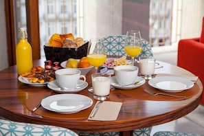 A breakfast table with plates, glasses, a bottle, and a basket of bread and fruit. - S Bento Residences Porto sao Bento (Porto)
