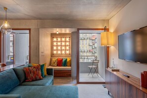 Un salon moderne avec un canapé, un téléviseur et une vue sur les immeubles à travers une porte vitrée.