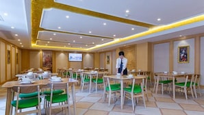 A hotel dining area with multiple tables and chairs, a television screen, and a waiter. - Vienna International Hotel (Enshi)