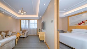 A hotel room with a sofa, a small table, a TV, and a bed. - Vienna International Hotel (Enshi)