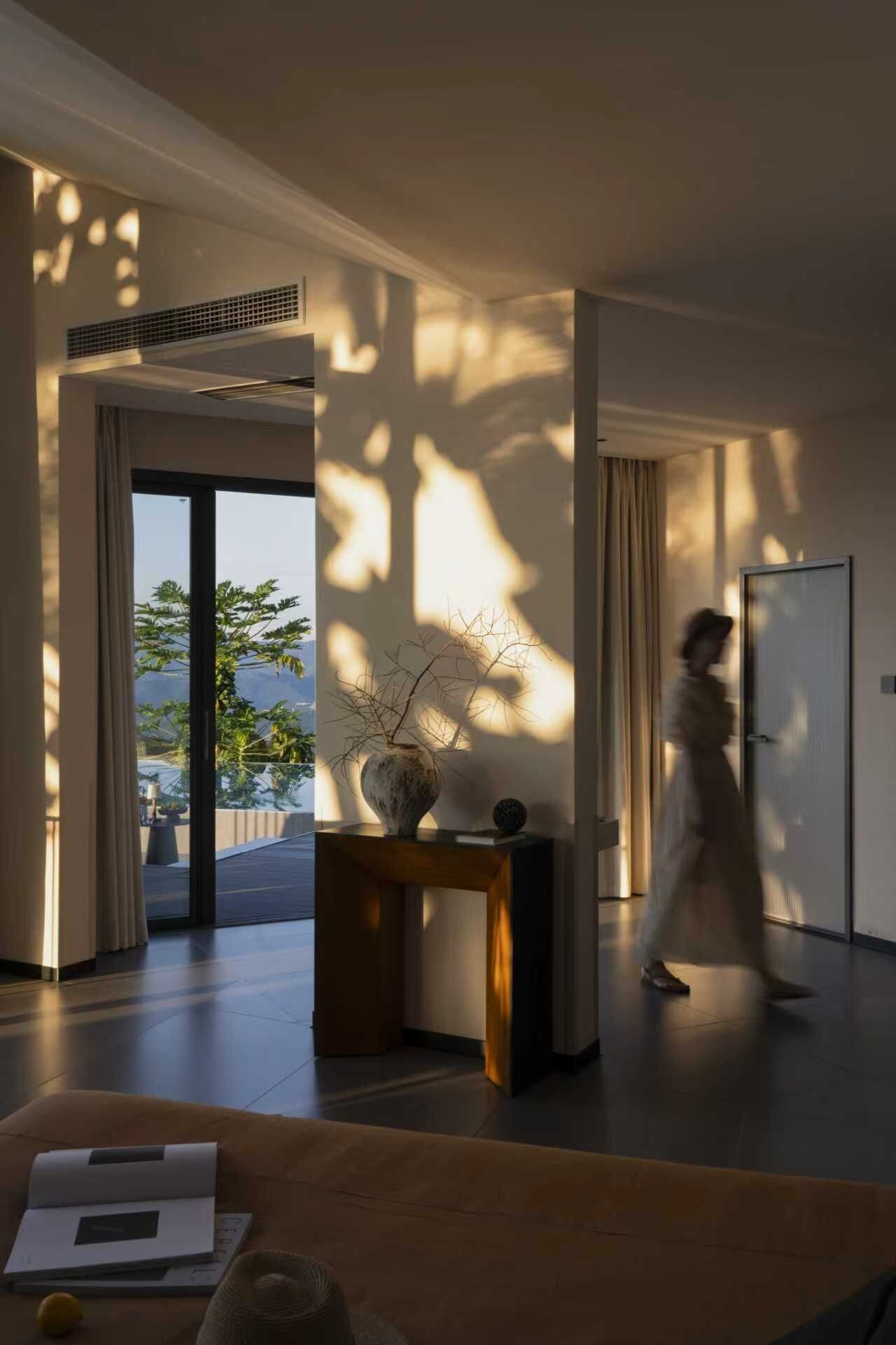 Ein modernes Interieur mit einem großen Fenster, einer Vase auf einer Konsolentisch und einer Person, die vorbeigeht.