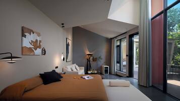 A modern bedroom with a large bed, a bedside table, a floor lamp, and a view of the outdoors through a sliding door.
