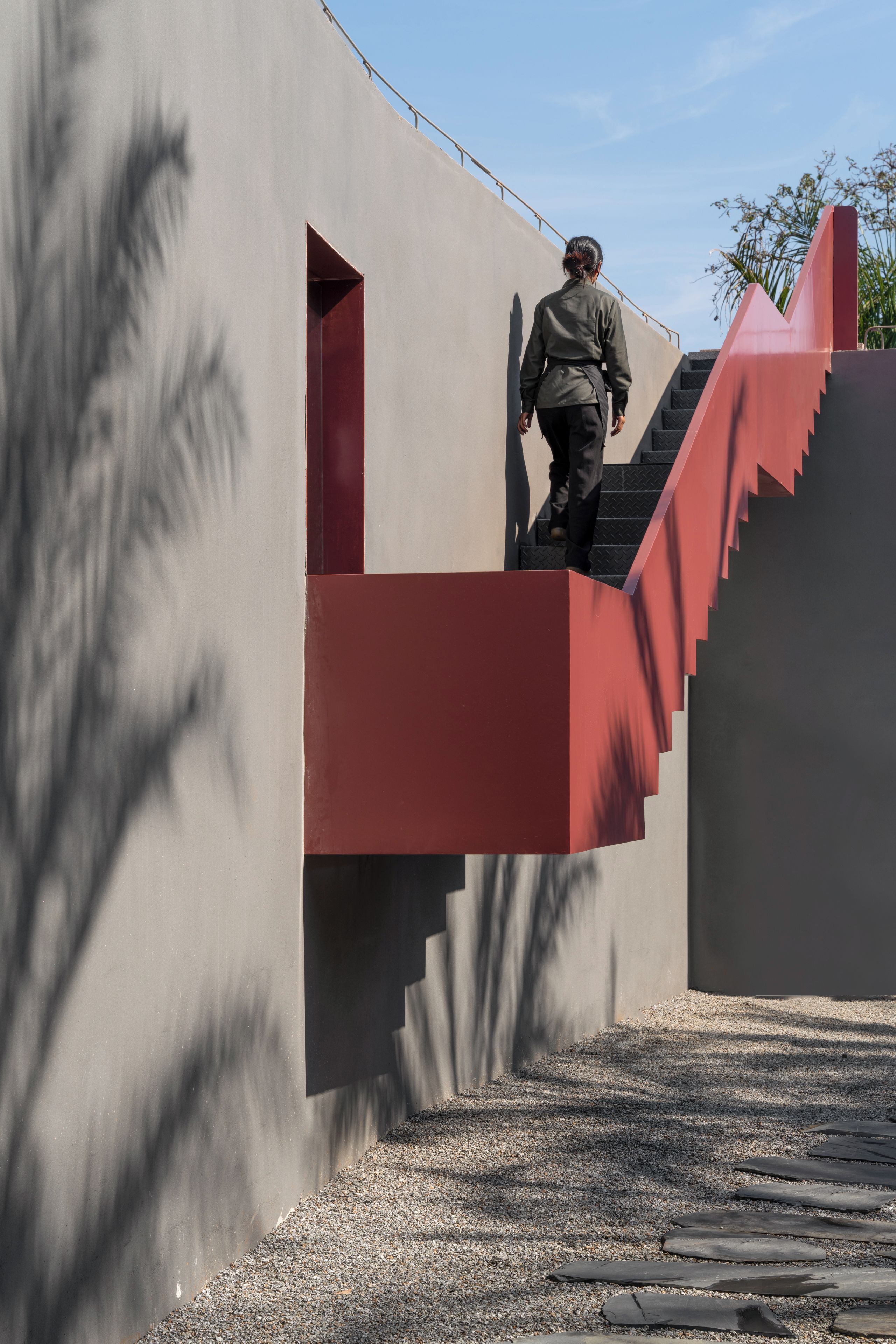 A person ascending a red staircase with a grey wall in the background.