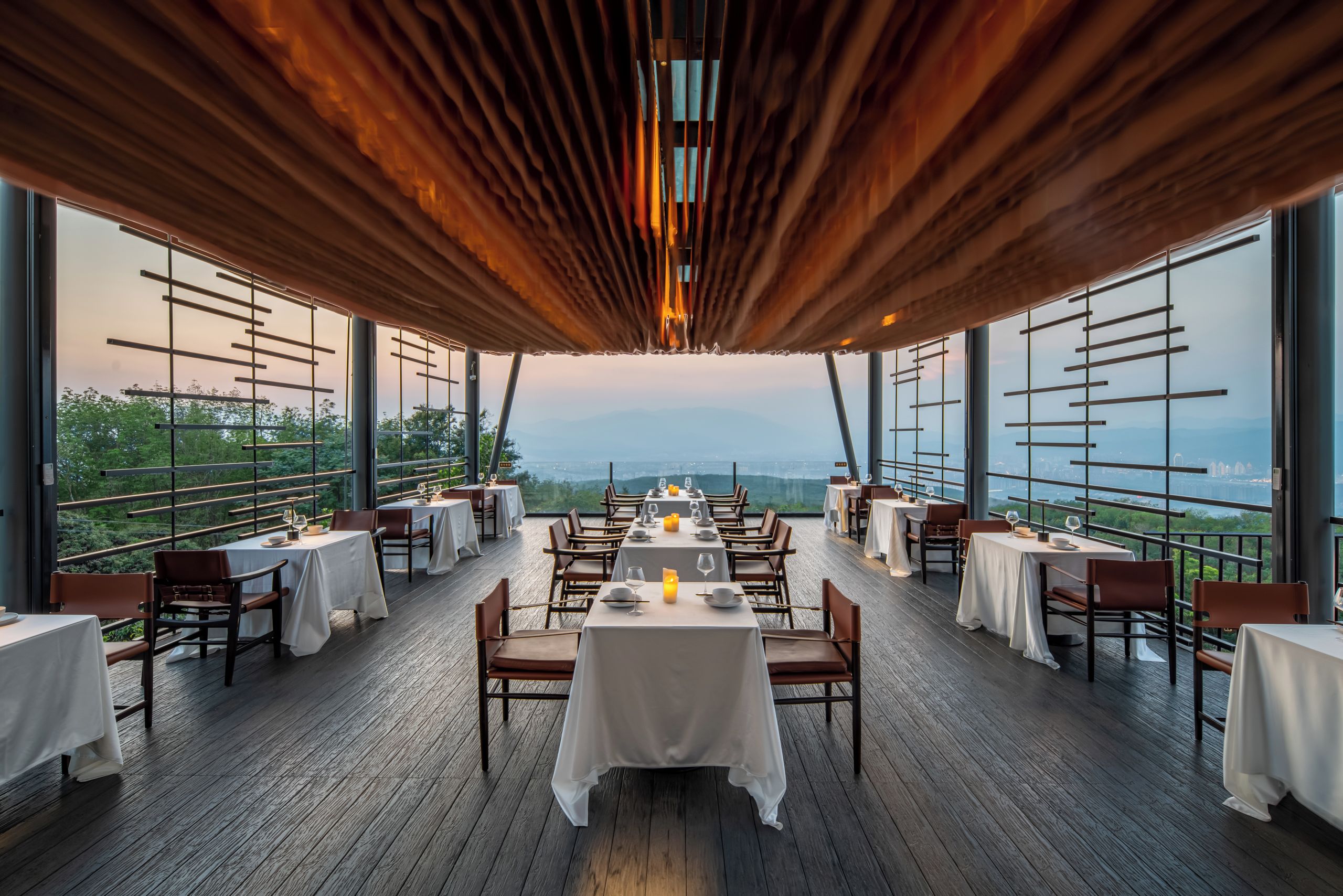A restaurant with a wooden deck, white tablecloths, and a view of the mountains.