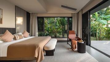 A modern bedroom with a large bed, a seating area with a chair, and a view of lush greenery outside.