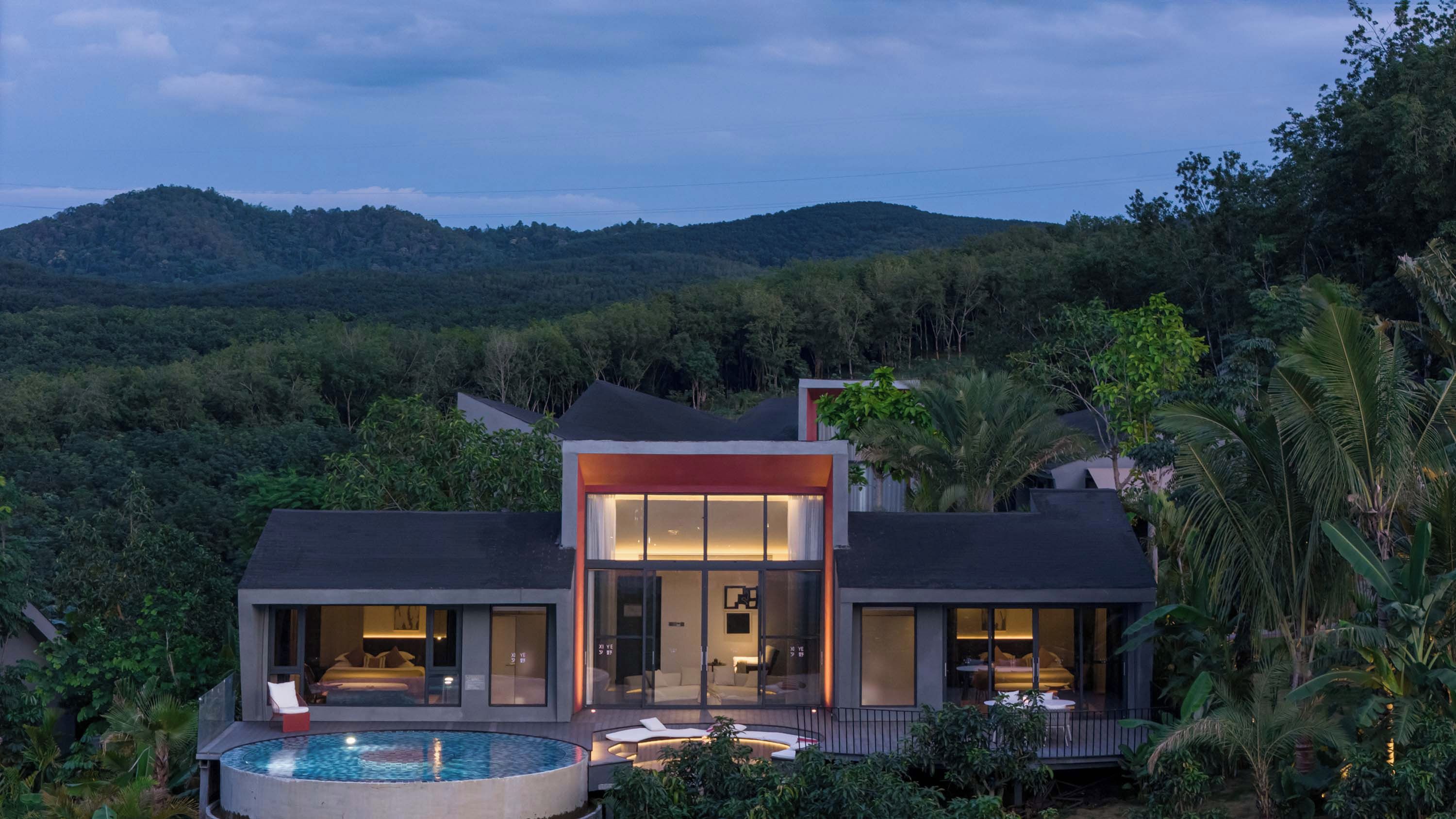 A modern house with a swimming pool, large windows, and a view of the surrounding forest.