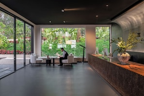 A modern reception area with a receptionist, large windows, and a view of a garden. - XiyeSeclusionResortHotel (Xishuangbanna Dai)