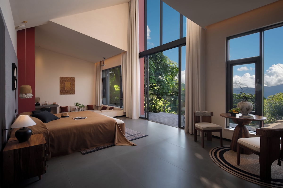Ruime slaapkamer met een groot bed, een zithoek en een balkon met uitzicht op groen en bergen.