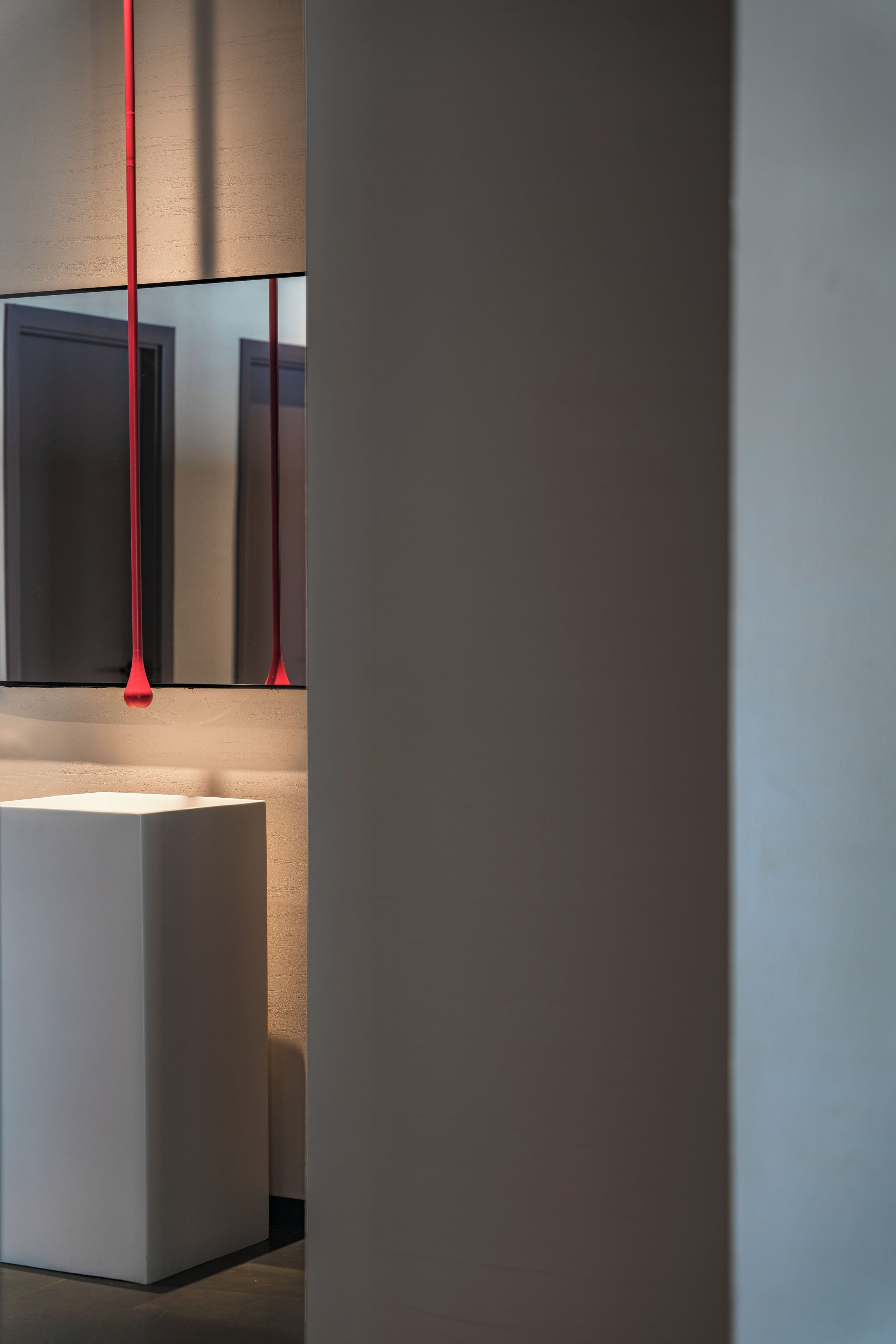 A modern bathroom with a minimalist design, featuring a white sink and a red light fixture.