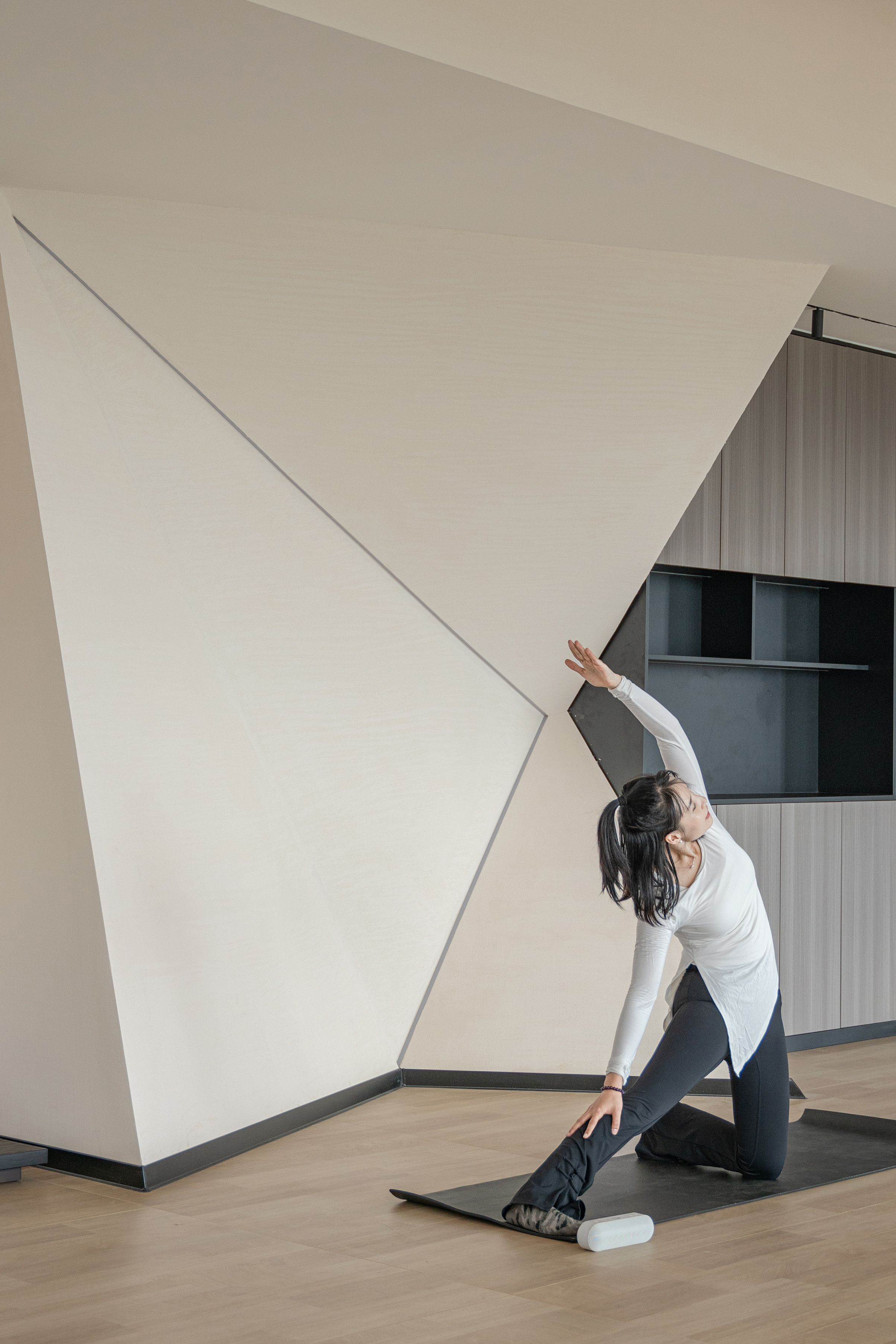 Eine Person führt eine Yoga-Pose auf einer Matte in einem Raum mit modernem Design durch, inklusive schräger Decke und Holzboden.